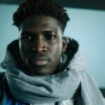 Close-up portrait of a man in winter clothing, indoors with a scarf and serious expression.